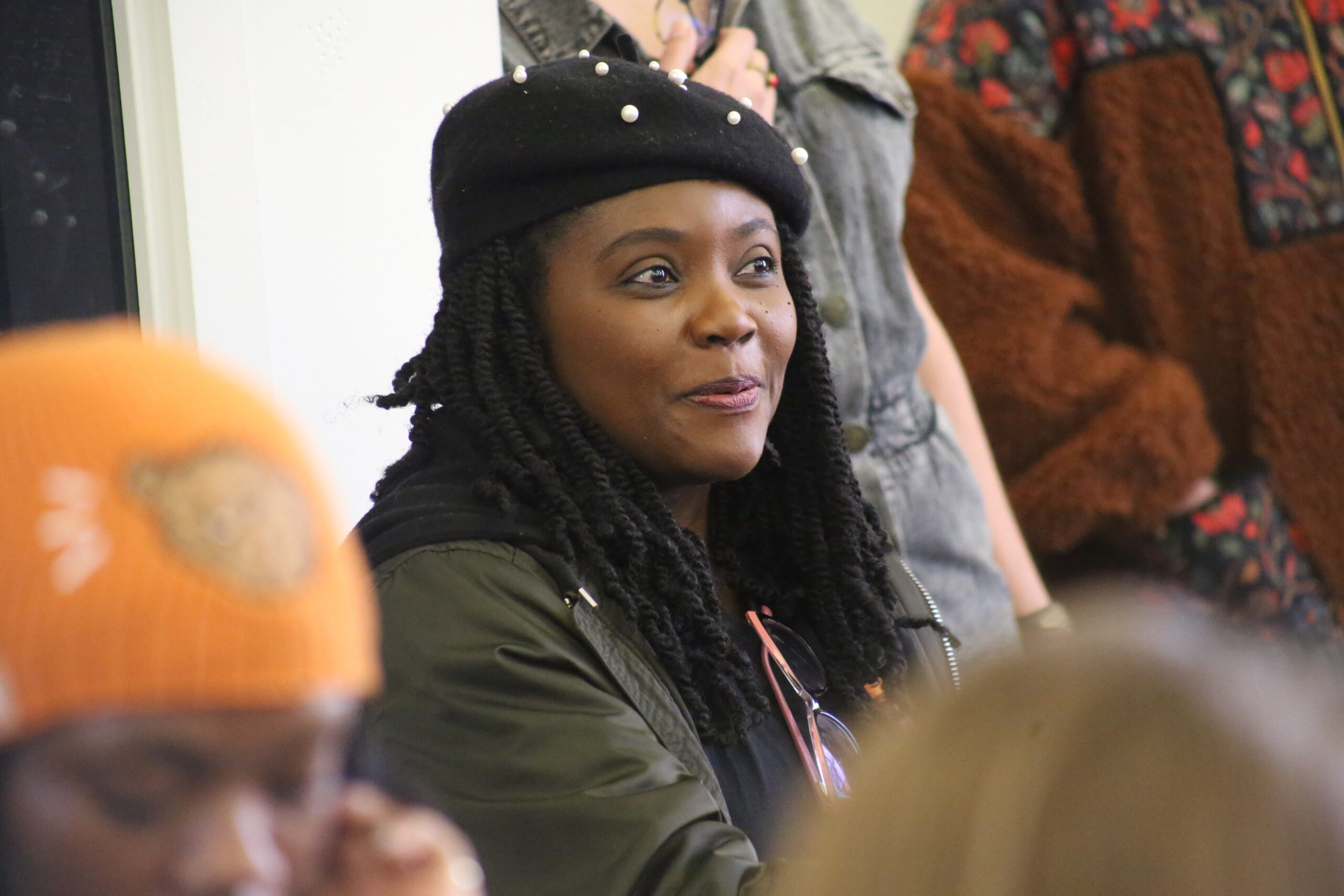 5D042020 A young woman in a cap sits among others in an audience. Focus is on her face and she's slightly smiling.